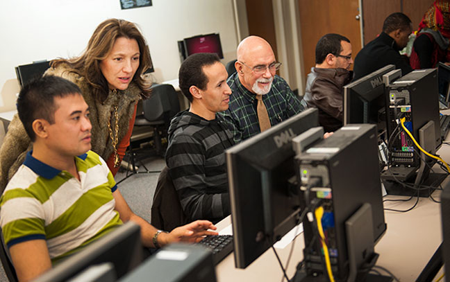 a professor leans down to show a student something on a screen in a classroom