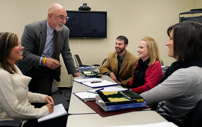 a professor leaning on a table talking to students during a class