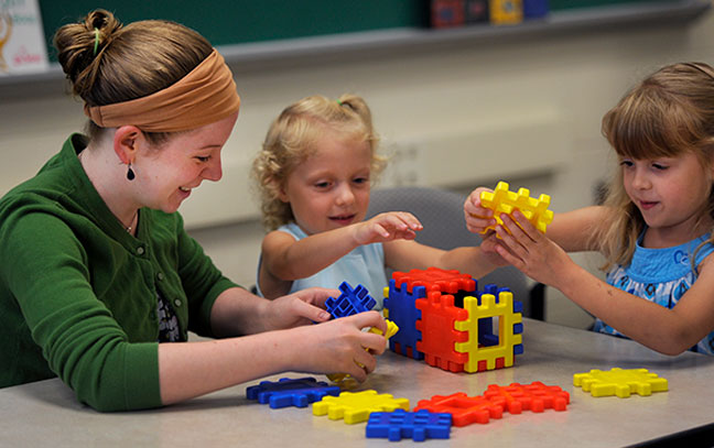 a female student works with small children with toys in a preschool