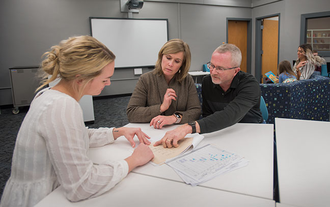 three people seated at a table look at documents together