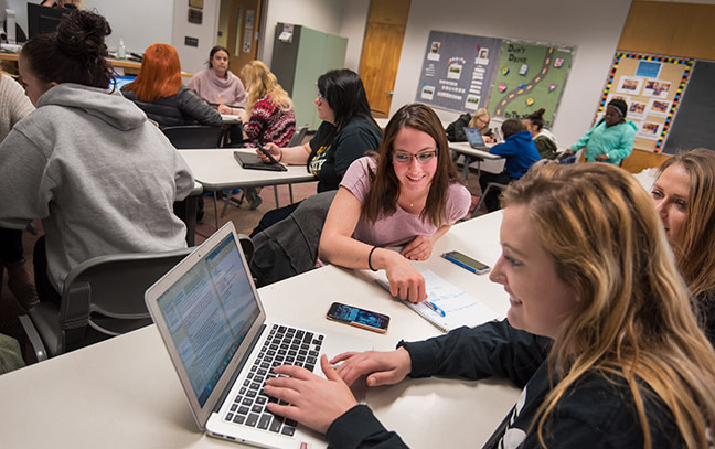 in a busy room, three students look at a computer screen