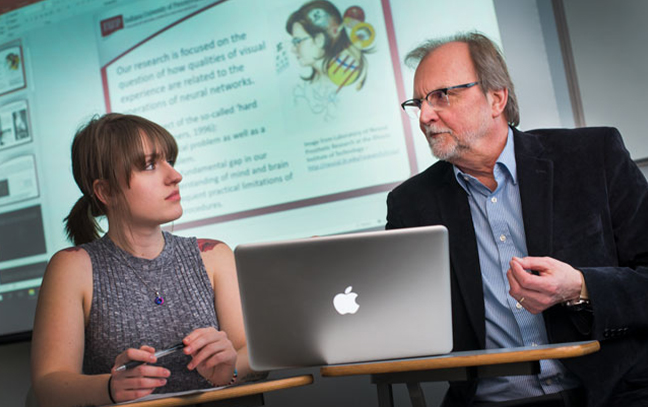 a student is seated at a table with her professor talking to him