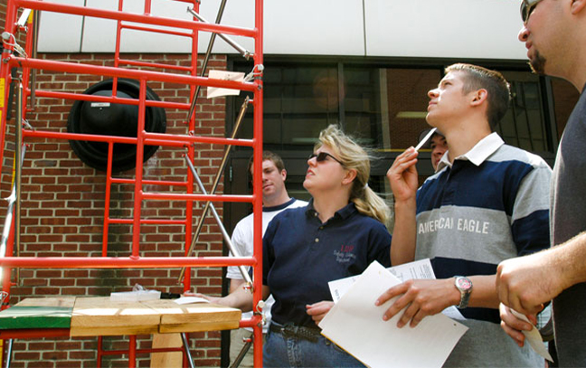 a group stands looking at and analyzing scaffolding and something out of the image