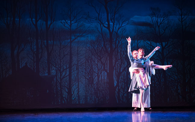 two dancers performing on a stage with forest background