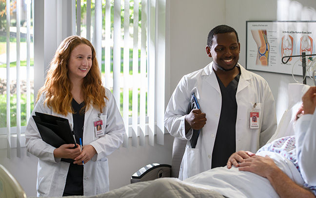 Two nursing students talk with a patient in a hospital bed