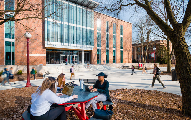 exterior of kophick hall from the oak grove with students sitting at tables