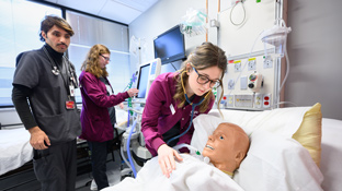 a nursing student checks on a medical simulation patient in a hospital room setting