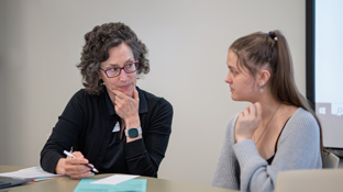 a female professor talks to a student while seated at a table together