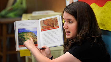 A student teacher holds up a book and points to its illustration while discussing it. 