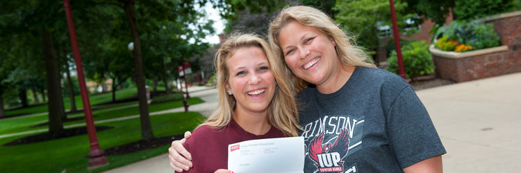 A mother and daughter hug in the Oak Grove as they celebrate the daughter's acceptance into IUP