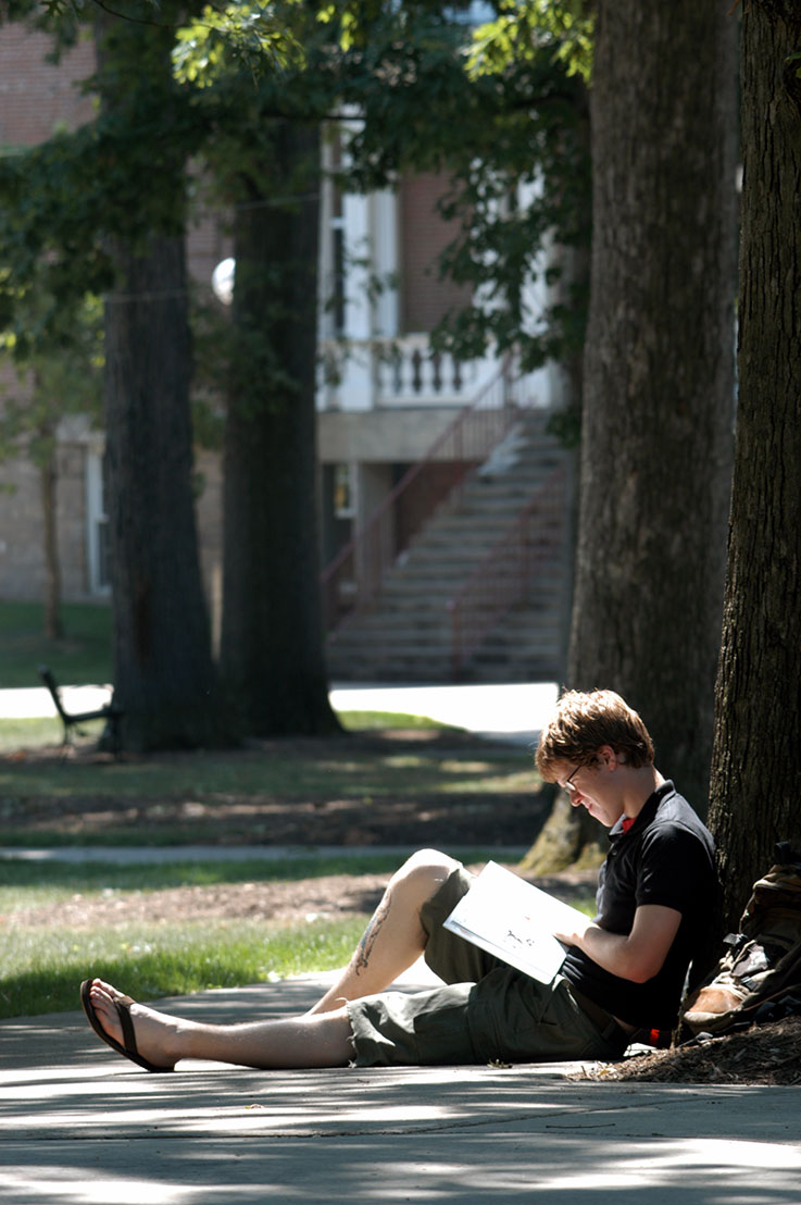Student studying under a tree in the Oak Grove 