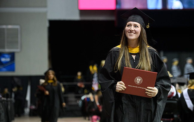 a smiling student holds her diploma 