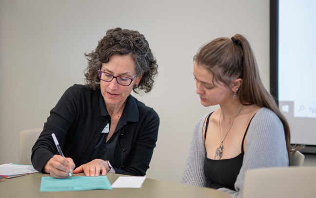 a professor and student sitting next to each other going over papers at a table