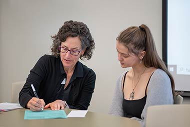 a professor and student sitting next to each other going over papers at a table