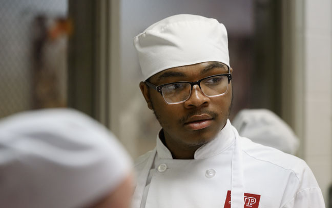 a photo of a young man facing slightly off camera wearing a chef's hat and uniform