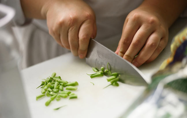 a white cutting board with two hands cutting green beans with a chef's knife