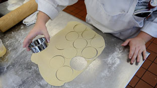 a chef uses a cookie cutter to cut circles in rolled out dough