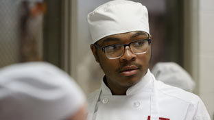 a culinary student in a chef's outfit and apron looking to the right of the image