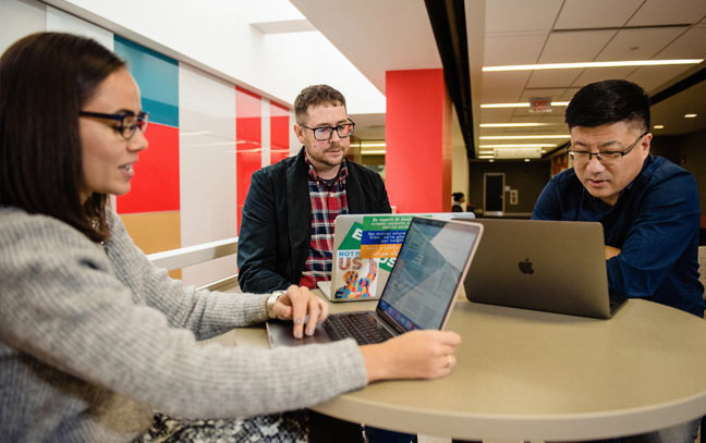 three people sitting at a small round table all looking at their laptops
