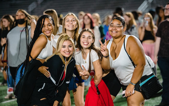 group of 5 female students smiling for the camera during an event on the football field