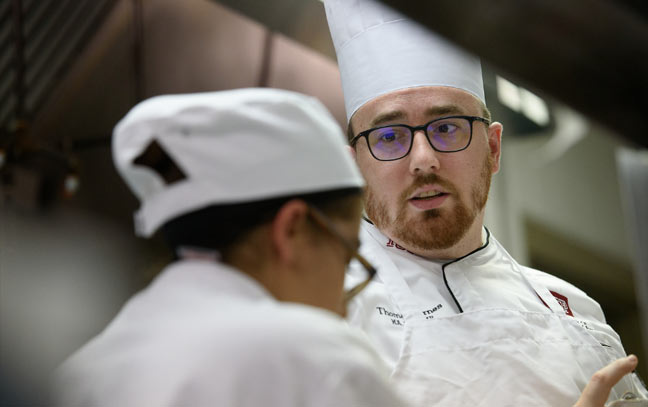 a chef instructs a student in a kitchen