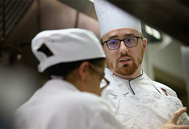 a chef instructing a student in a kitchen