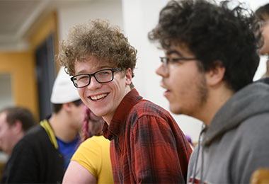 two young men in a group talking to one another and laughing