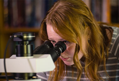 a young woman looking into a microscope