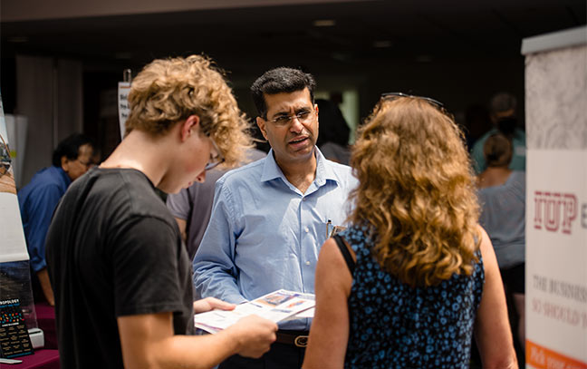 a man speaking to two students at a college fair