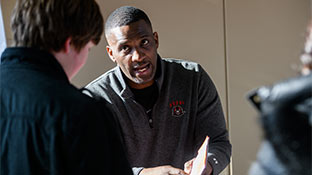 Two people sitting at a table talking.  The person in the foreground is facing away from the camera.