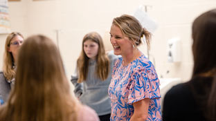 a woman in a pink and blue shirt stands smiling in a group of students