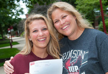 a young woman and her mother smile together at the camera while presenting a printed letter from IUP