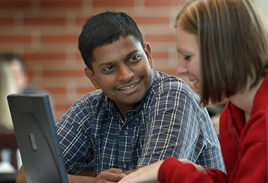 a man and woman sitting at a laptop computer together having a conversation