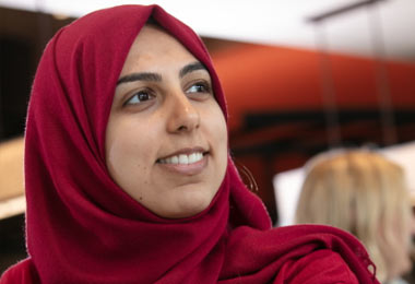 A student wearing a red hijab smiles while facing the right of the image