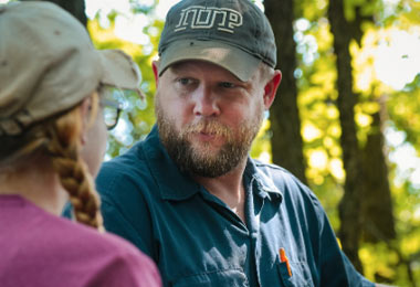 A professor standing in the woods talking with a student