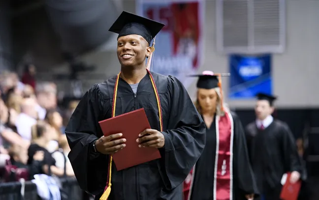 a student in cap and gown carries his diploma during commencement