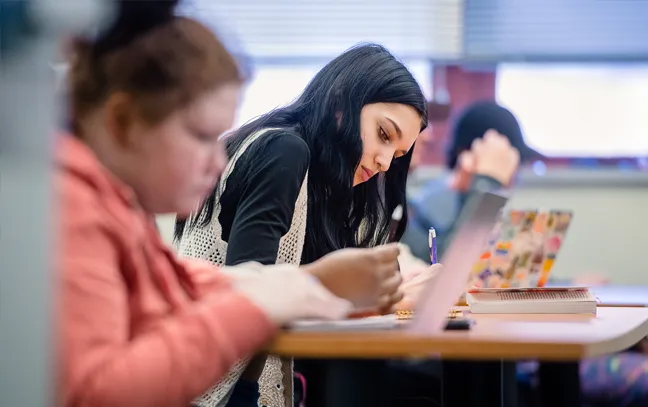 three students in a row of desks facing toward the right while focusing on their laptops and study materials