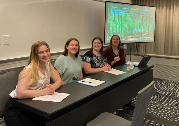 4 students sitting at a long table for their panel presentation