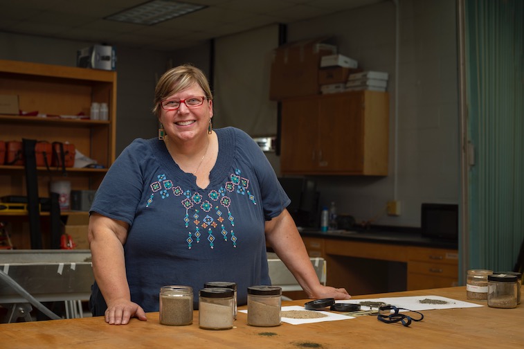 Dr. Katie Farnsworth standing in front of a lab table with sand samples