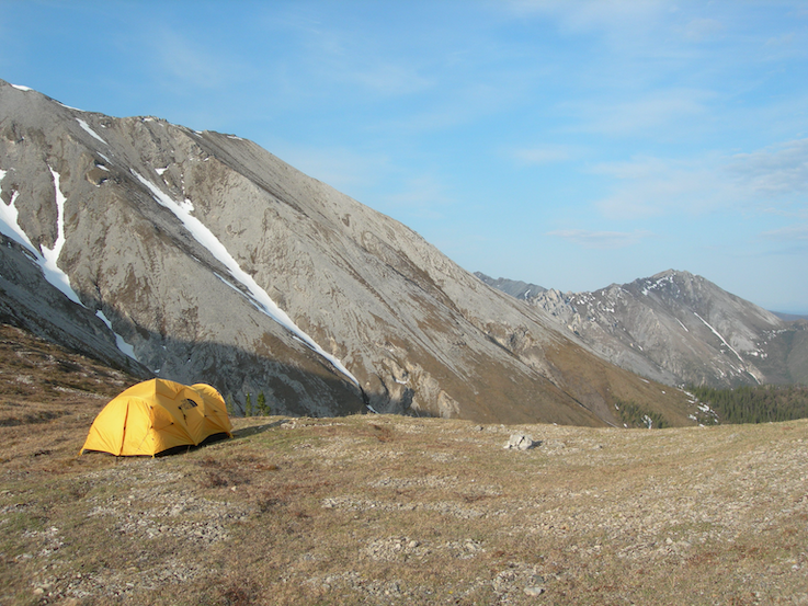 Photograph of a yellow tent in a remote area of Alaska, with a large rocky mountain in the background.