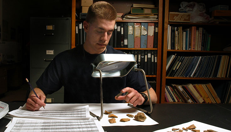 An Archaeology student looks at rock chips and some arrowheads in a lab.