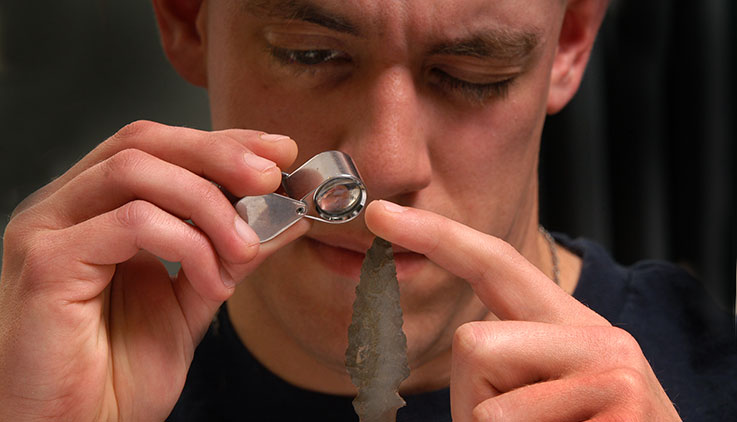 An Archaeology student looks at rock chips and arrowheads in a lab