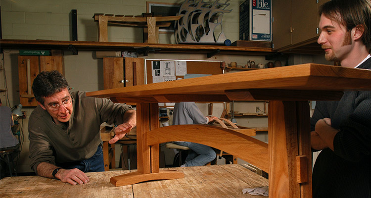 A professor a give advice to a student who has crafted an artistic wood furniture piece