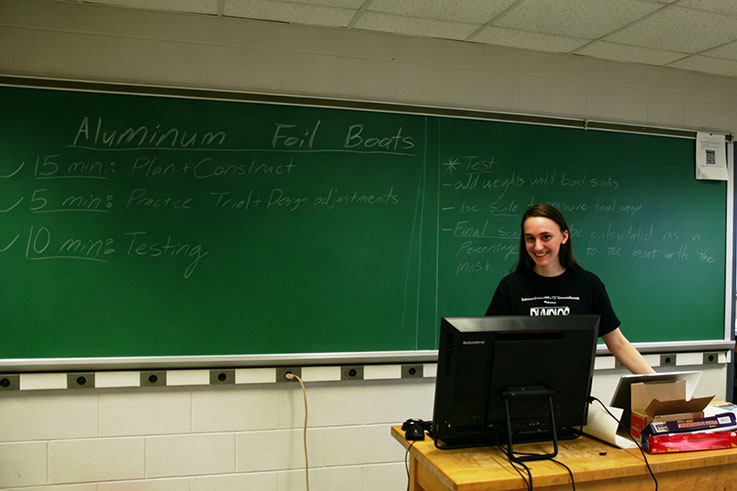 Mariah standing in front of the black board during the 2019 IUP Physics Olympics