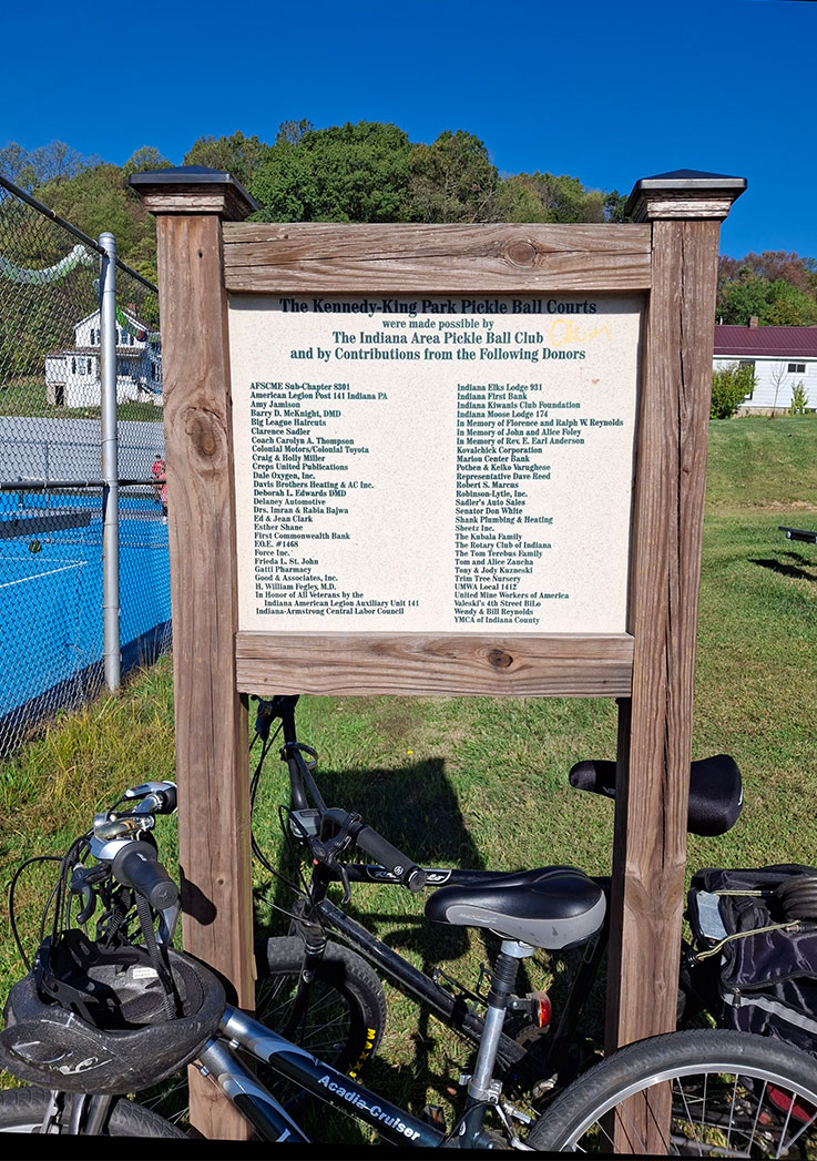 A wooden outdoor sign at the Kennedy-King Park Pickleball Courts gives thanks to the Indiana Area Pickleball Club and to the donors, with a list below it.