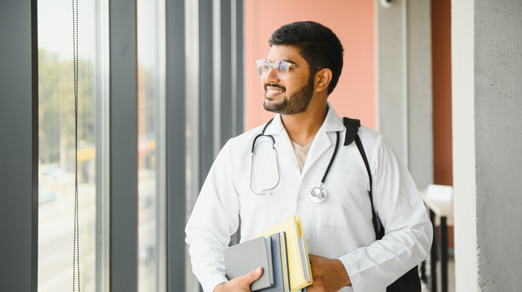 man in a doctor coat looking out a window in a hospital