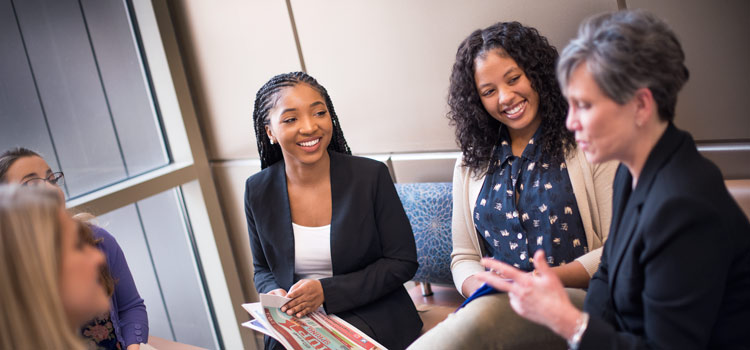A group of female strategic communication students sit in a group with their professor
