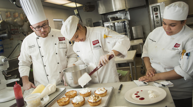 two culinary students watch as a third fills pastry cups with filling