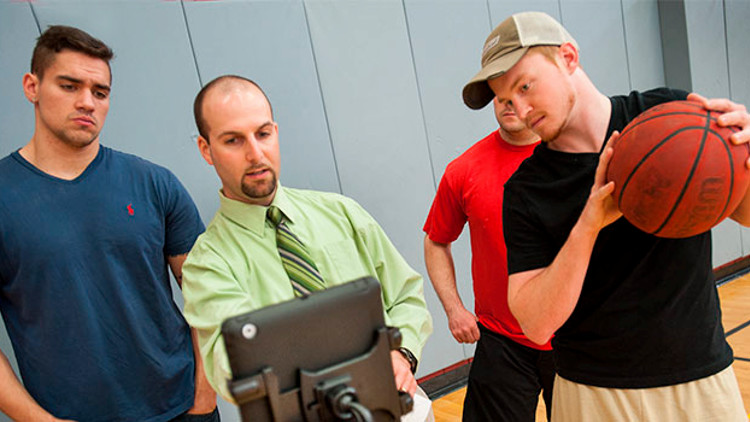 Students in CWE listen to a professor using a laptop as one student holds a basketball