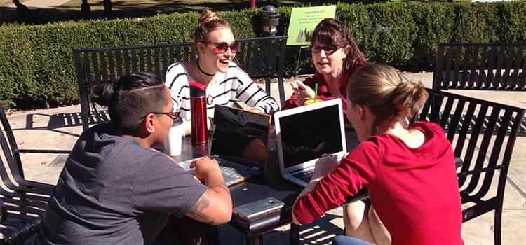 Four English graduate students study together at a table outside the library